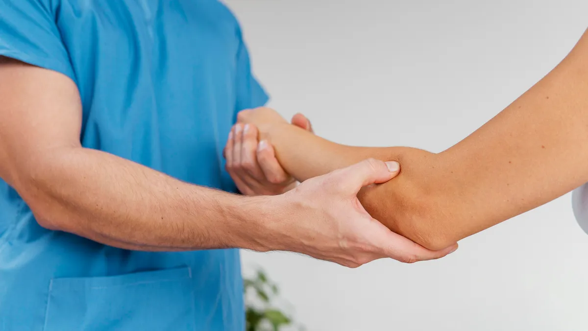 osteopathic therapist checking female patient's elbow joint movement